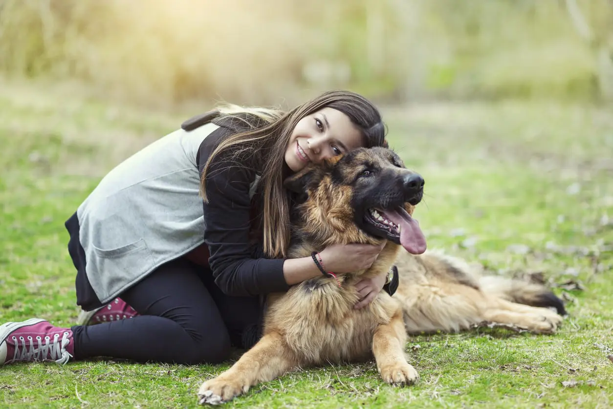 a woman in athletic gear giving her dog a hug in the grass