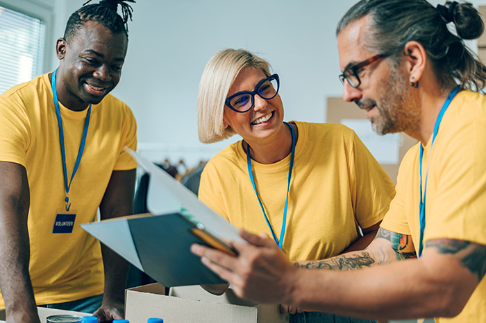 Three volunteers working in non-profit are reading direct mail and wearing matching yellow shirts with blue lanyards