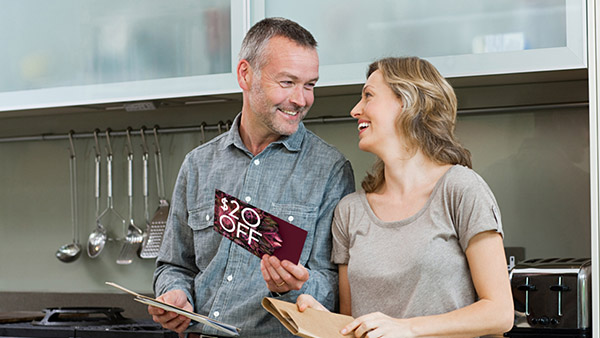 A couple reading direct mail postcards in the kitchen while looking into each others eyes and smiling