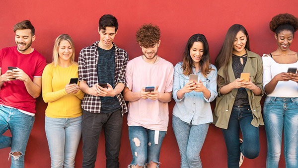 A group of Gen Z people standing against a red wall while looking at their phones