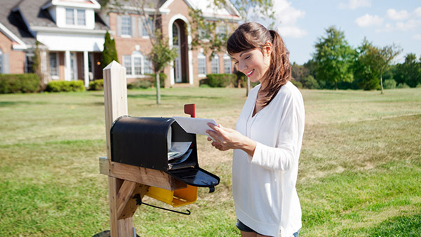 Woman in front of a mansion opening her mail in her front yard