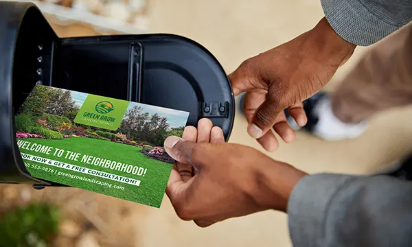 A person opening their mailbox with a postcard that says welcome to the neighborhood