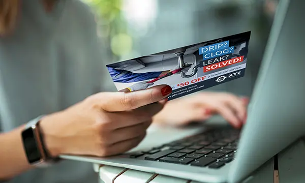 A person on a latop filling out information from a direct mail postcard for a plumbing service