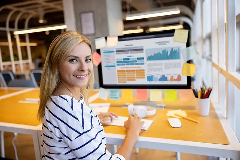 a blonde-haired woman wearing stripes working in a modern office on a computer with graphs on the screen