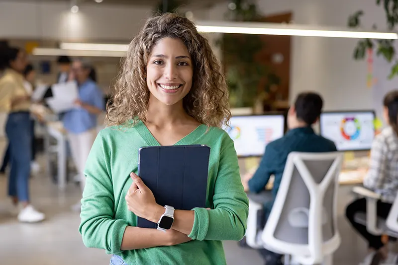 Woman wearing a green shirt in a modern, busy office while holding a tablet close