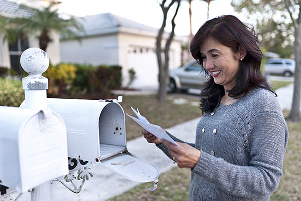 Woman in her 40s reading mail by two white mailboxes in the suburbs
