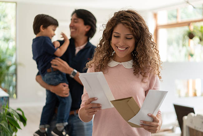 Woman reading direct mail at home with family in the background